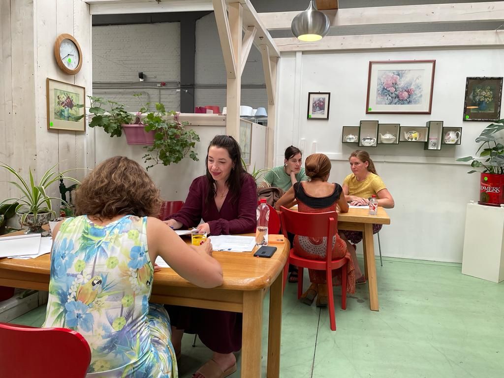 Aan de voorste tafel zit Talissa tegenover een testpersoon (helemaal links in beeld). Aan de achterste tafel zitten Eline (links) en Madelon (rechts) tegenover een andere testpersoon.